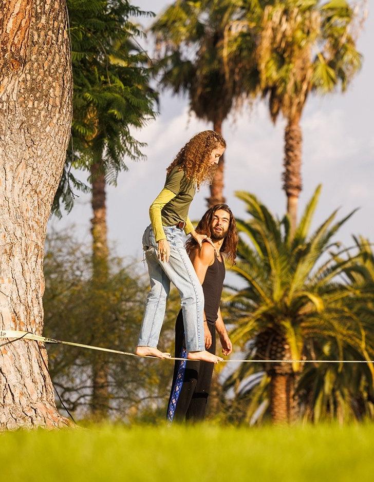 a student practices on the mounds slackline while holding a friend's shoulder